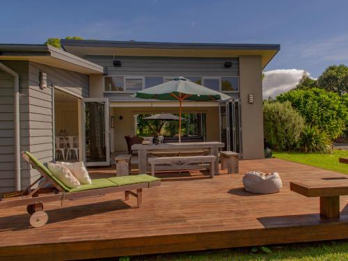 a wooden deck with a table and an umbrella at Cooks Getaway - Cooks Beach Holiday Home in Cooks Beach