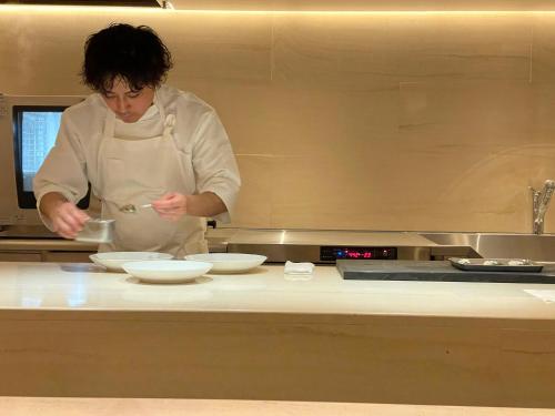 a chef standing in a kitchen preparing food at まえばしガレリアArt residence & Hotel in Maebashi