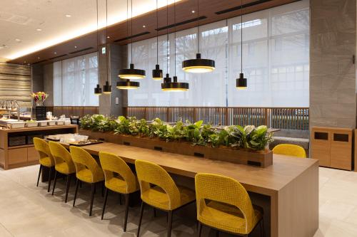a dining room with a long table and yellow chairs at Shimanami PRIME HOTEL IMABARI in Imabari