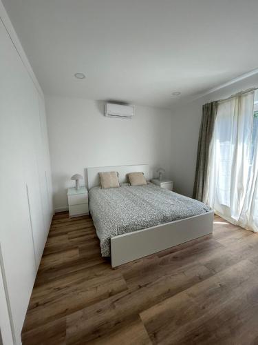 a white bedroom with a bed and a wooden floor at Apartamento Tronqueiras in Praia da Vitória