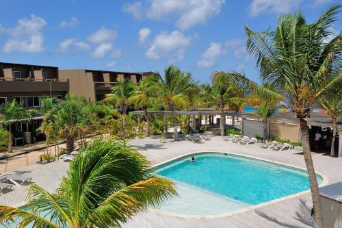 a pool with palm trees and chairs and a building at Eden Beach Resort - Bonaire in Kralendijk