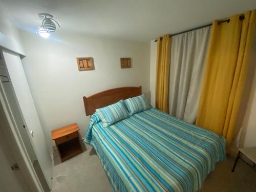 a small bedroom with a bed with a striped bedspread at Departamento Peñuelas in La Serena
