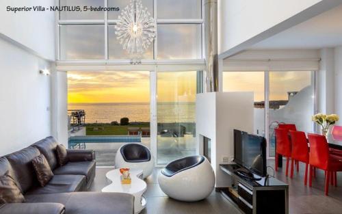 a living room with a couch and a television with a view of the ocean at BLUE CORAL BEACH VILLAS three exclusive villas - Poseidon - Nautilus - Oceanos - and - Baby Coral bungalow in Coral Bay
