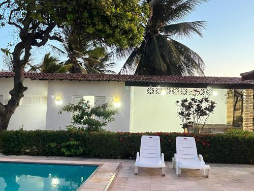 two white chairs next to a house with a swimming pool at Praia Marina Suite - Morro Branco in Beberibe
