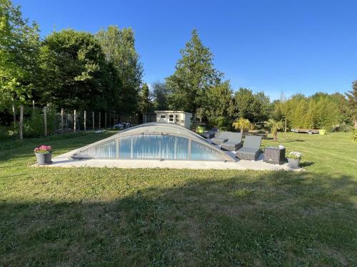 une maison en verre dans un parc avec des bancs dans l'herbe dans l'établissement Maison avec Piscine, à Semblançay