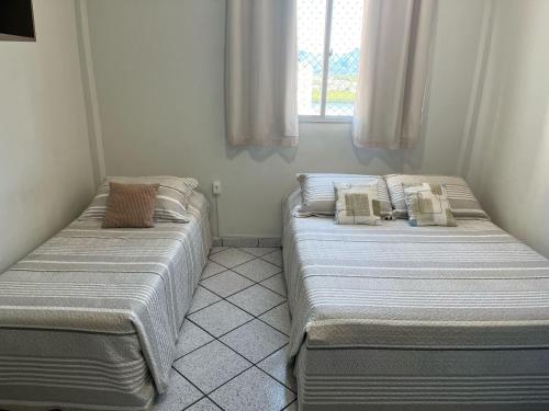 two twin beds in a room with a window at KITNET ACONCHEGANTE A 3 MINUTOS DA PRAIA in Guarapari