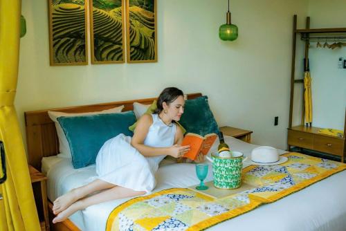 a woman laying on a bed reading a book at Blue Tropical House Hội An in Hoi An