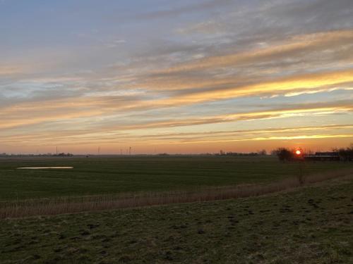 a field with the sun setting in the horizon at Ferienwohnung Watt'n Ausblick in Simonsberg