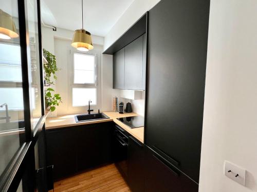 - une cuisine avec des placards noirs et un évier dans l'établissement Appartement de charme - Place Victor Hugo - Paris 16e, à Paris