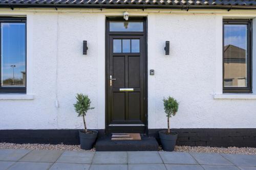 a black door on a white house with two plants at Almara- Cosy cottage in fife in Fife