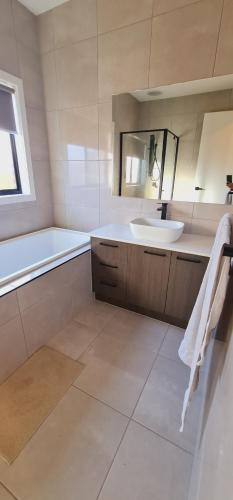 a bathroom with a sink and a tub and a mirror at Stay in Tarneit West Melbourne in Tarneit