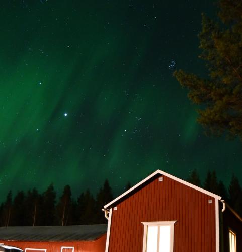 a red barn under a green sky with the stars at Arctic Hearts - Kleines Schwedenhaus im Wald am See in Jörn