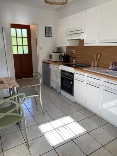 une cuisine avec des armoires blanches et une table et des chaises dans l'établissement Escapade en normandie avec soins bien être, à Le Chambray