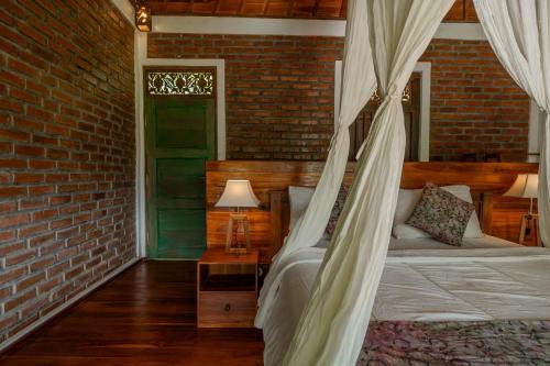 a bedroom with a canopy bed and a brick wall at Saridevi Ecolodge in Jatiluwih