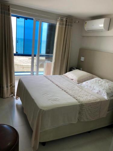 Un dormitorio con una cama y una ventana grande. en Cobertura frente mar 2 suítes, en Itapema