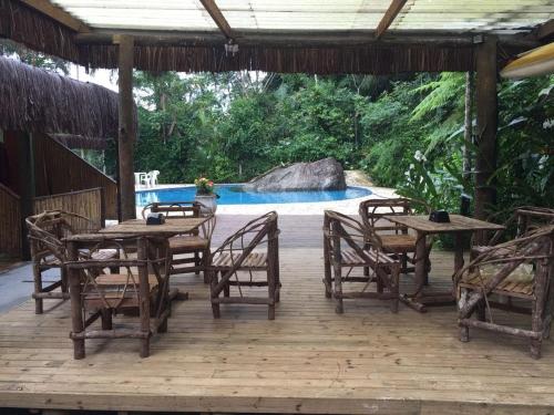 a wooden deck with tables and chairs and a pool at Pousada Toka do Lula - Oficial in Peruíbe