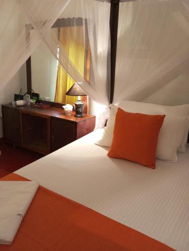 a bedroom with a bed with an orange pillow and a desk at Dishari Tangalle in Tangalle