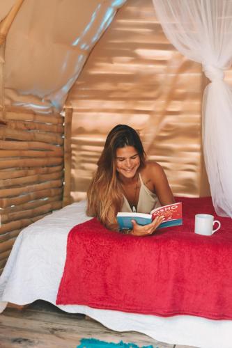 a woman laying on a bed reading a book at Camping Green house in Saquarema