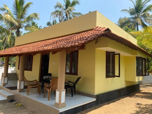 a small yellow house with chairs and a table at Gaya beach hacienda in Irimbranallūr