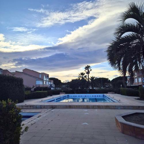 une piscine avec un palmier et un ciel nuageux dans l'établissement T2 Lumineux tout équipé avec piscine, parking privé et plage à 300m, à Palavas-les-Flots