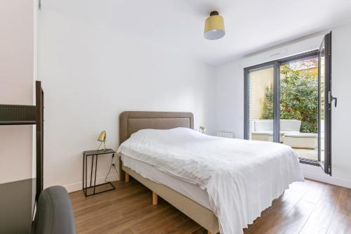 a white bedroom with a bed and a window at L'Escapade Paris in Le Kremlin-Bicêtre