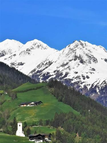 a snow covered mountain with a house in a green field at Lampeterhof in Matrei in Osttirol