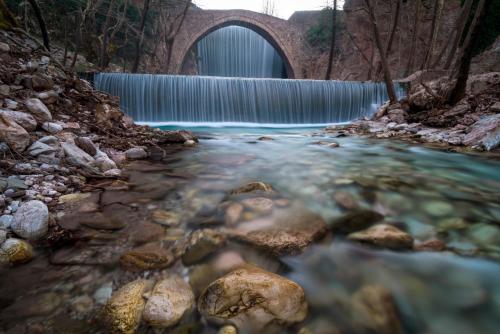 a bridge over a river with a waterfall in the background at Το σπίτι στο χωριό in Tríkala