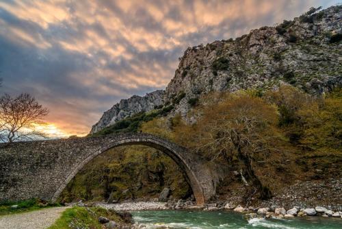 an old bridge over a river with a mountain at Το σπίτι στο χωριό in Tríkala