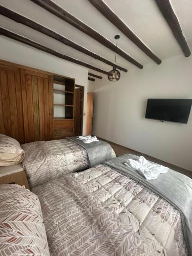 a bedroom with two beds and a flat screen tv at Hotel Sol de la Montaña Villa de leyva in Villa de Leyva