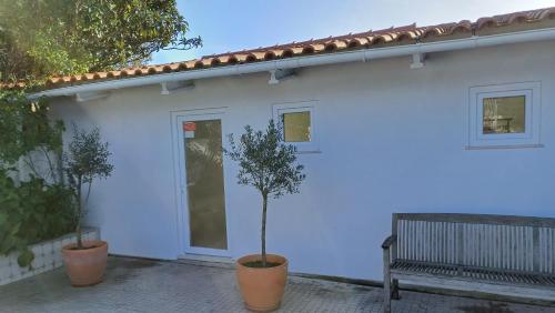 a white building with two potted trees next to a bench at Quinta da pêra rocha in Alcobaça
