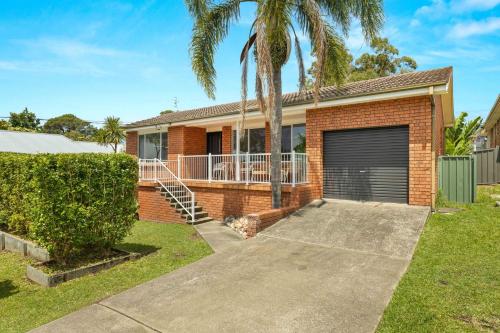 a brick house with a garage and palm trees at Tide's Edge by Experience Jervis Bay in Vincentia