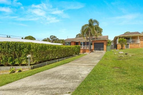 a house with a hedge in front of a driveway at Tide's Edge by Experience Jervis Bay in Vincentia