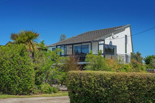 a white house with windows and bushes at Kina Beach House in Tasman