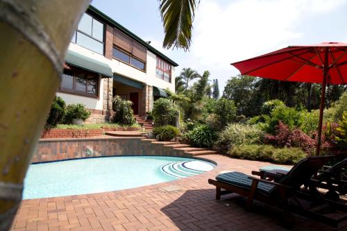 a swimming pool with a red umbrella and a house at Ridgeview Lodge in Durban