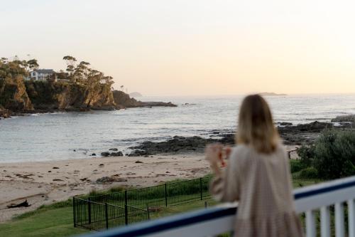 a woman standing on a balcony looking at the beach at Beachfront Shack Malua Bay - Dog Friendly with EV Fast Chgr in Malua Bay