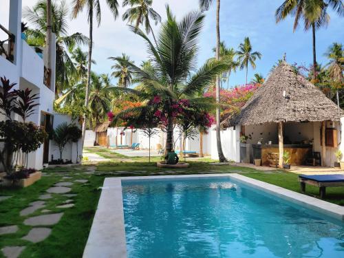 a pool in front of a house with palm trees at Mambo Cabana in Pwani Mchangani