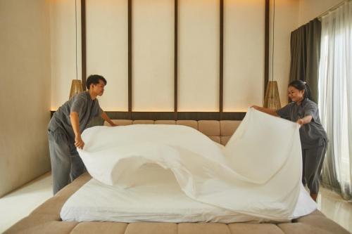 two people making a large bed in a room at Ahimsa Beach in Jimbaran