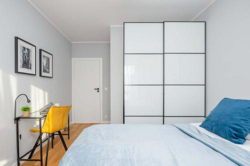 a white bedroom with a bed and a yellow chair at Elegant Apartment in Warsaw with Parking and Desk for Remote Work by Noclegi Renters in Warsaw