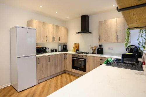 a kitchen with a white refrigerator and wooden cabinets at Vinmar Very Special Bungalow In Charming Area Of Wales By StayStaycations in Pengam