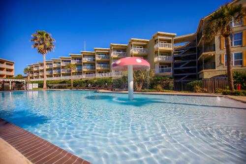 a swimming pool with an umbrella in front of a building at Sea-Renity Heated pools steps to the beach in Galveston