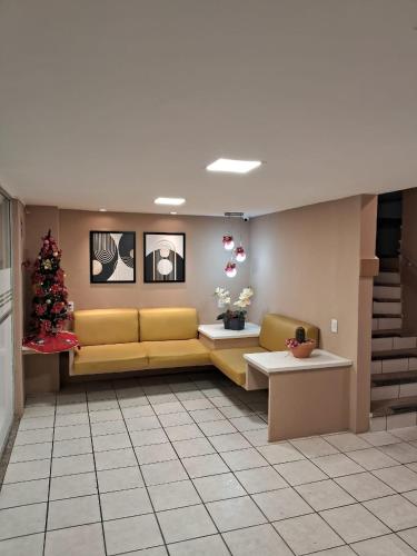 a waiting room with a yellow couch and a christmas tree at Apê Espaçoso e Econômico - Pertinho da Praia in Recife
