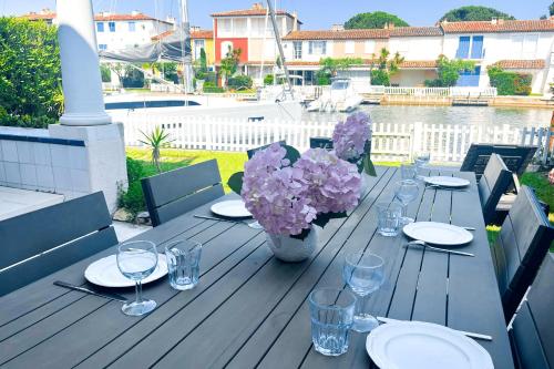 - une table en bois avec des assiettes, des verres et des fleurs dans l'établissement Wide house with WIFI and AC a terrace a garden and a 12m mooring, à Grimaud