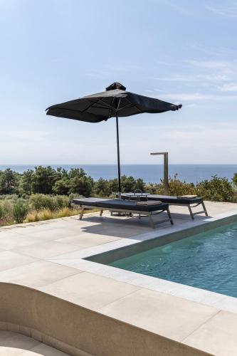 a table with an umbrella next to a swimming pool at Fari Stone Villas in Skala Marion