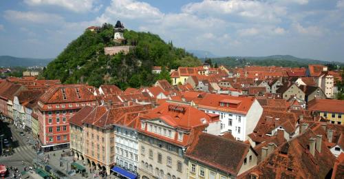 a city with buildings and a hill with a clock tower at Holzmeisterhütte Teichalm-Sommeralm in Sankt Kathrein am Offenegg