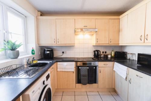 una cocina con armarios de madera y encimeras negras en 12FWC, 2 Bedroom Apartment, Sleeps 4, Free Parking, Town Centre Location, en Swindon