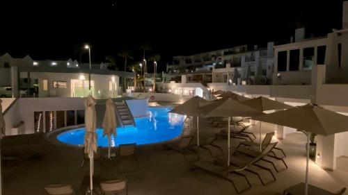 a swimming pool with chairs and umbrellas at night at Kikere Studios in Puerto del Carmen
