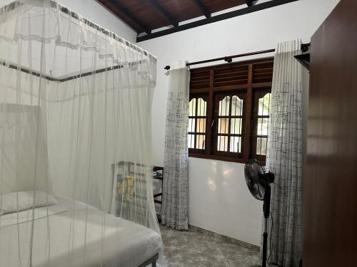 a bedroom with a bed with white curtains and a window at White Swan Villa Unawatuna in Unawatuna