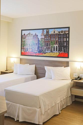 two beds in a hotel room with a painting on the wall at Hotel Amsterdam Montes Claros in Montes Claros