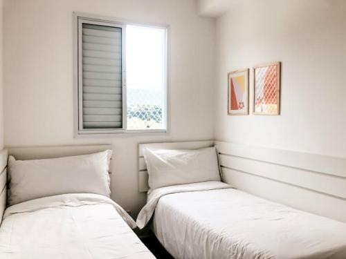 two beds in a white room with a window at Jardim das Palmeiras II - Multipropriedade in Ubatuba