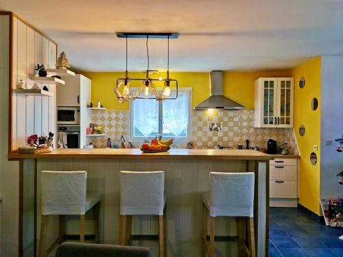 une cuisine avec des murs jaunes et un îlot de cuisine avec des chaises blanches dans l'établissement Maison de vacances aux portes de l'Ardèche, à Saint-Julien-en-Saint-Alban